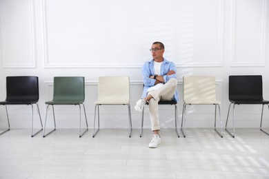 Photo of Man sitting on chair and waiting for appointment indoors