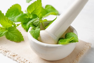 Photo of Fresh lemon balm leaves and pestle in mortar on white wooden table, closeup