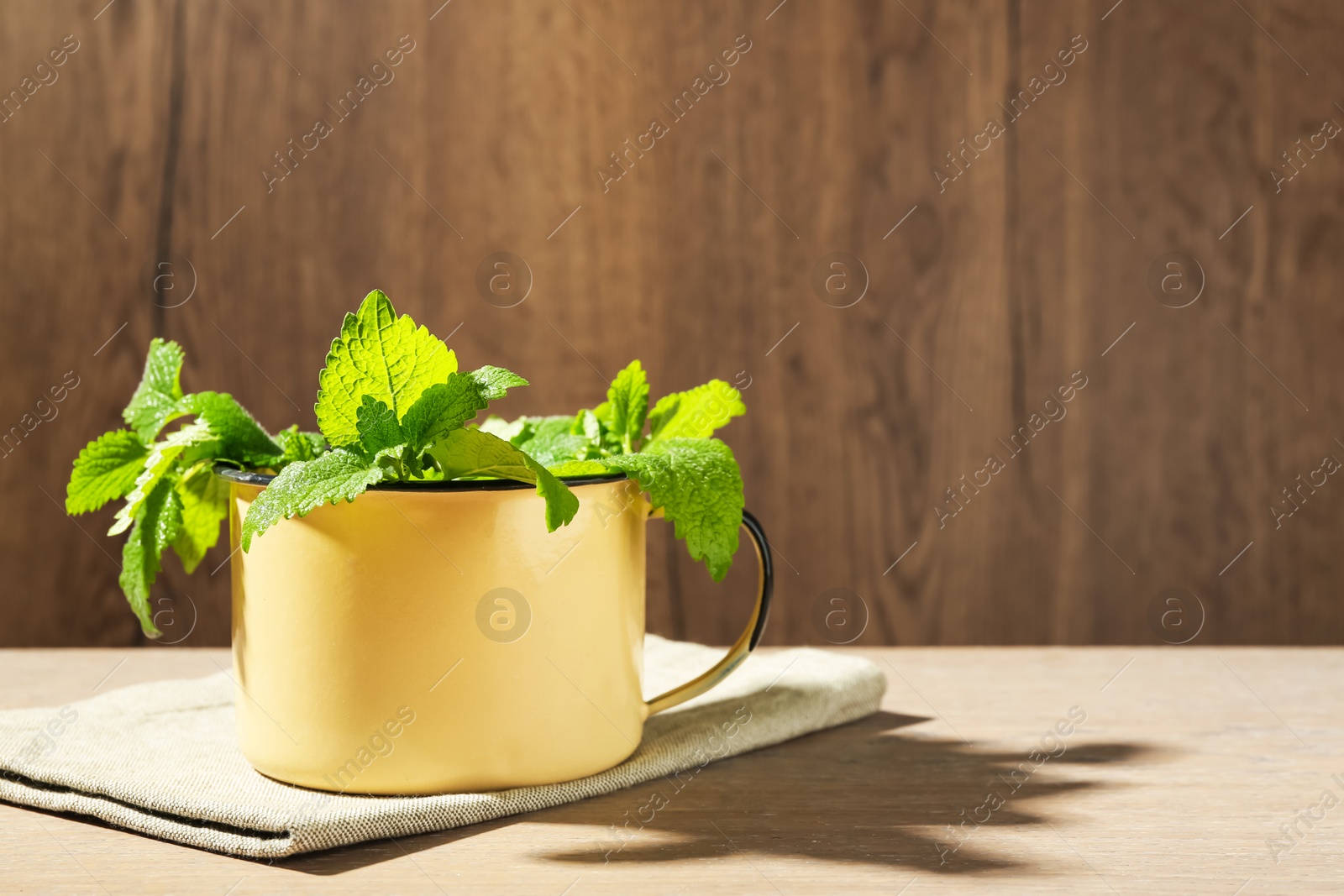 Fresh lemon balm leaves in mug on wooden table. Space for text Photo of Fresh lemon balm leaves in mug on wooden table. Space for text