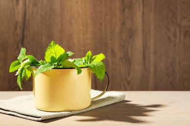 Photo of Fresh lemon balm leaves in mug on wooden table. Space for text