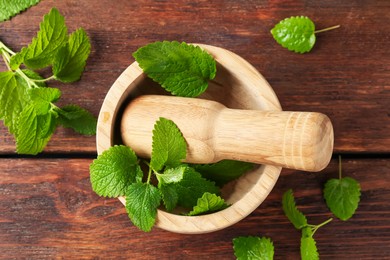 Photo of Fresh lemon balm leaves, pestle and mortar on wooden table, flat lay