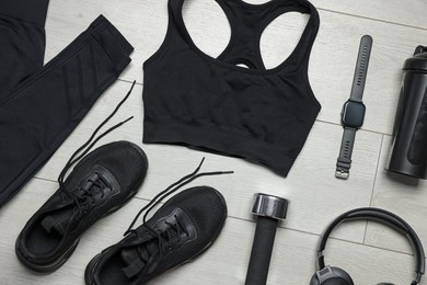 Photo of Sportswear, sneakers, wrist watch, headphones and dumbbell on floor, flat lay