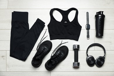 Photo of Sportswear, sneakers, wrist watch, headphones and dumbbell on floor, flat lay