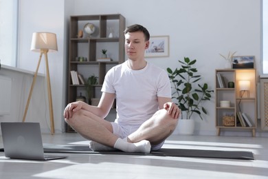 Photo of Man having online yoga class via laptop at home