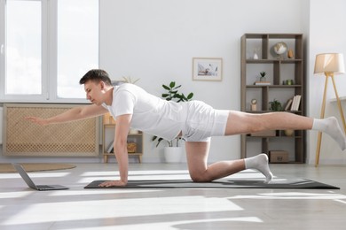 Photo of Man having online yoga class via laptop at home
