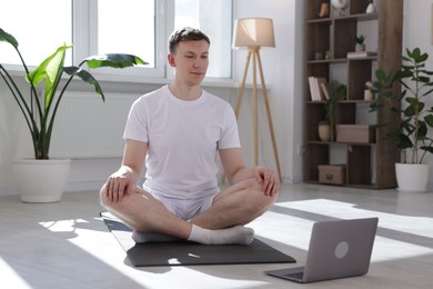 Photo of Man having online yoga class via laptop at home