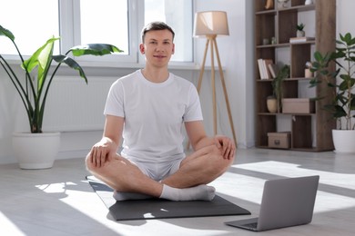 Photo of Man having online yoga class via laptop at home