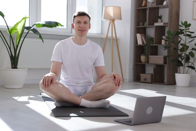 Photo of Man having online yoga class via laptop at home