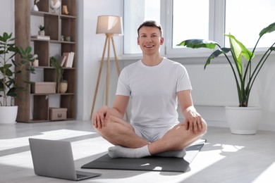 Photo of Man having online yoga class via laptop at home