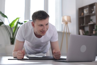 Photo of Man having online yoga class via laptop at home