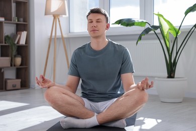 Photo of Young man practicing yoga on mat at home