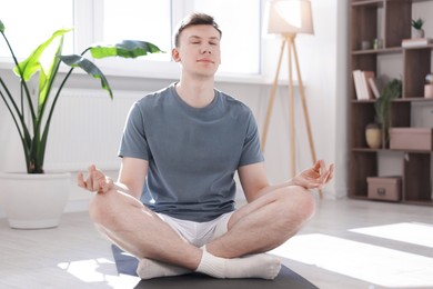 Photo of Young man practicing yoga on mat at home
