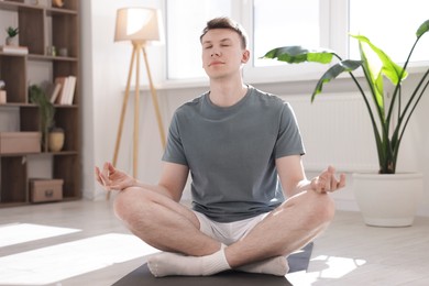 Photo of Young man practicing yoga on mat at home