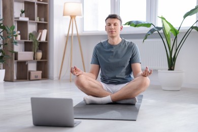 Photo of Man having online yoga class via laptop at home