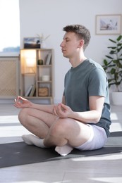 Photo of Young man practicing yoga on mat at home
