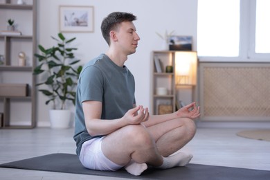 Photo of Young man practicing yoga on mat at home