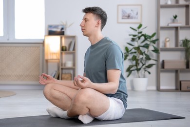 Photo of Young man practicing yoga on mat at home