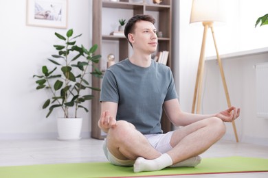 Photo of Young man practicing yoga on mat at home