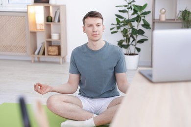 Photo of Man having online yoga class via laptop at home