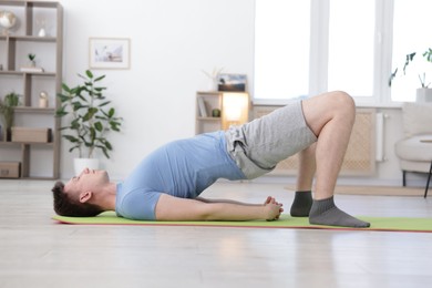 Photo of Young man practicing yoga on mat at home