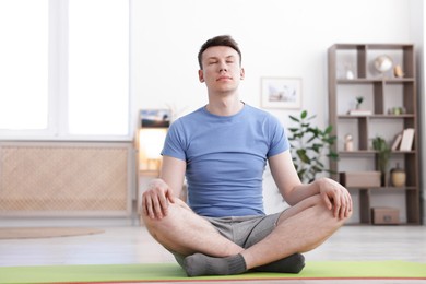 Photo of Young man practicing yoga on mat at home