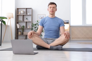 Photo of Man having online yoga class via laptop at home