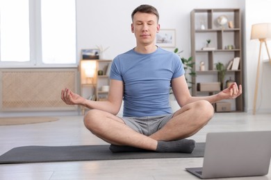 Photo of Man having online yoga class via laptop at home