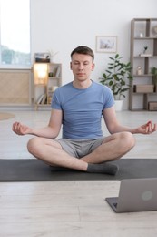 Photo of Man having online yoga class via laptop at home