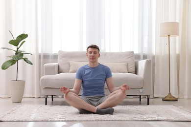 Photo of Young man practicing yoga on floor at home