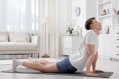 Photo of Young man practicing yoga on mat at home
