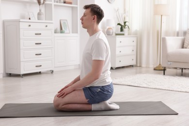 Photo of Young man practicing yoga on mat at home
