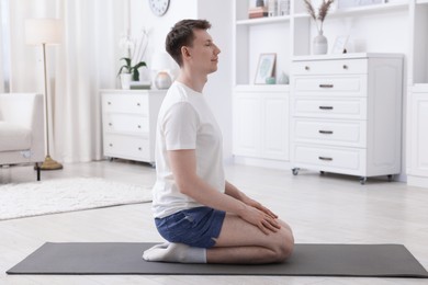 Photo of Young man practicing yoga on mat at home