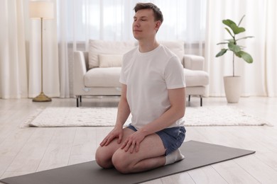 Photo of Young man practicing yoga on mat at home