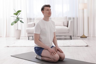 Photo of Young man practicing yoga on mat at home