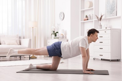 Photo of Young man practicing yoga on mat at home. Space for text