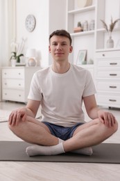 Photo of Young man practicing yoga on mat at home
