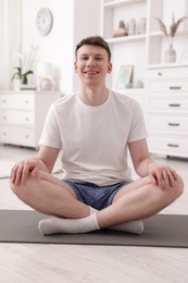 Photo of Young man practicing yoga on mat at home