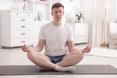 Photo of Young man practicing yoga on mat at home