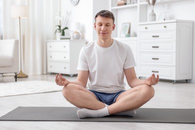 Photo of Young man practicing yoga on mat at home