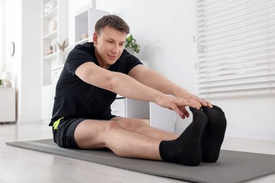Photo of Young man practicing yoga on mat at home