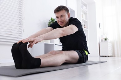 Photo of Young man practicing yoga on mat at home