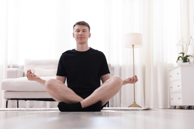 Photo of Young man practicing yoga on mat at home