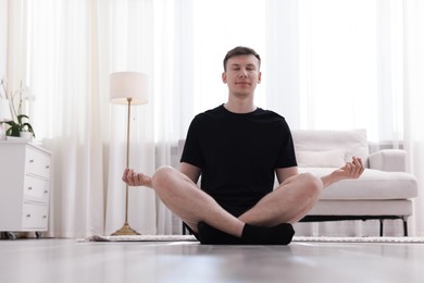Photo of Young man practicing yoga on mat at home. Space for text