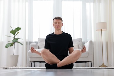 Photo of Young man practicing yoga on mat at home