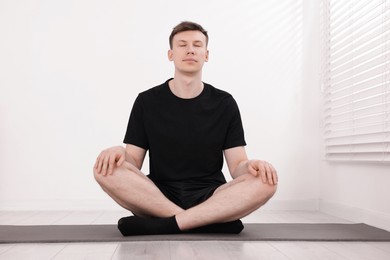 Photo of Young man practicing yoga on mat at home