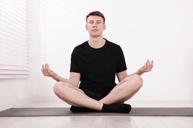 Photo of Young man practicing yoga on mat at home