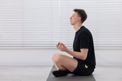 Photo of Young man practicing yoga on mat at home. Space for text