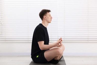 Photo of Young man practicing yoga on mat at home