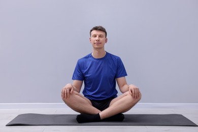 Photo of Young man practicing yoga on mat indoors
