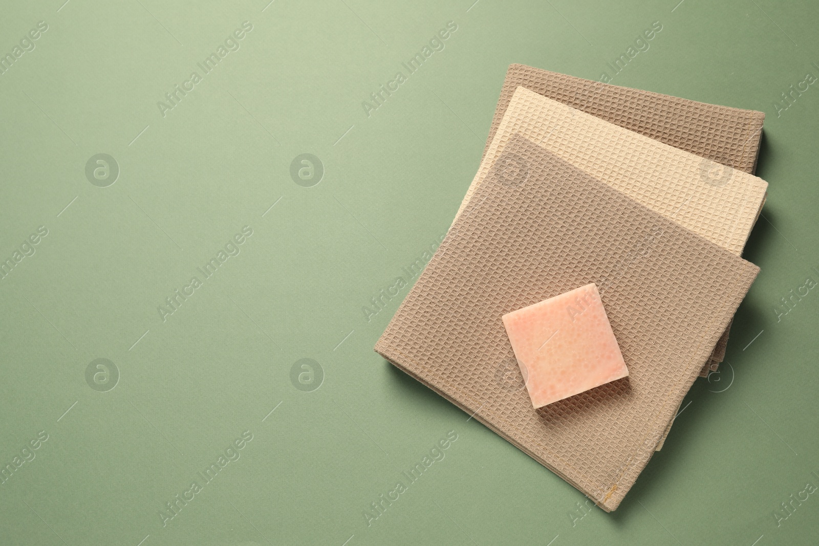 Photo of Clean waffle towels and soap bar on green background, top view. Space for text